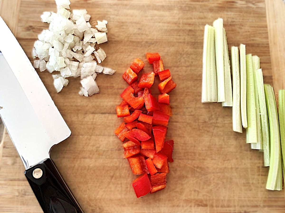chef knife and cutting board demonstrating different types of cuts with finely chopped onions, diced peppers and sliced celery