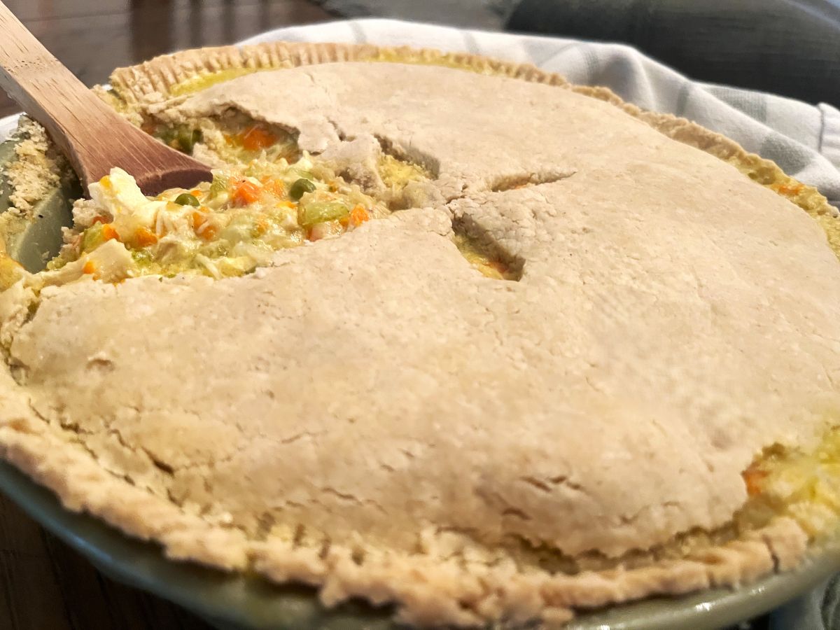 baked gluten free chicken pot pie in a pie dish, being served with a wooden spoon